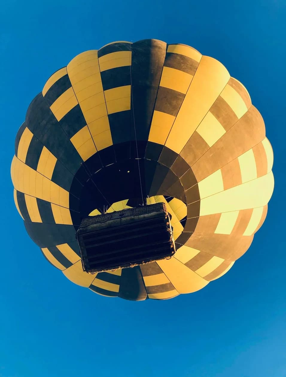 Looking up at a yellow and navy hot-air balloon against a clear blue sky