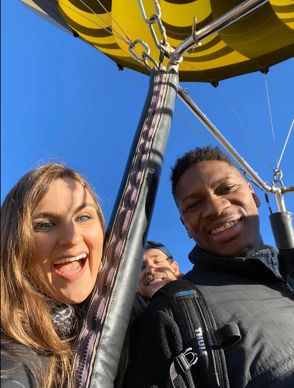 Two smiling passengers in a basket beneath a yellow hot-air balloon